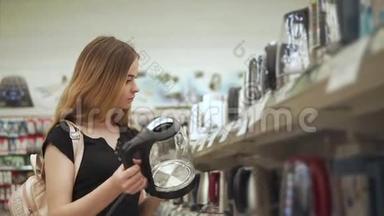 年轻漂亮的女人正在商店货架附近检查电热水壶的样品